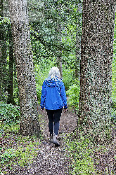 Blick von hinten auf eine Frau  die einen unbefestigten Weg durch den Watershed Forest Trail entlang geht; Delta  British Columbia  Kanada