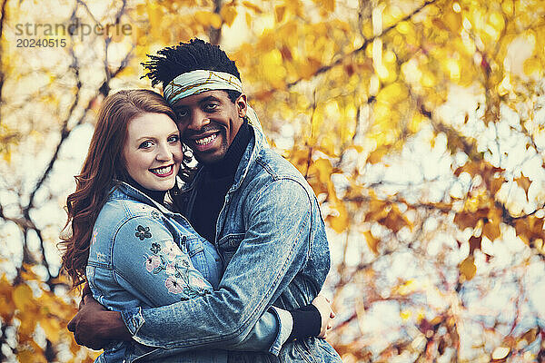 Nahaufnahme eines verheirateten Paares gemischter Abstammung  das sich umarmt und in die Kamera lächelt  während es bei einem Familienausflug im Herbst in einem Stadtpark schöne Zeit miteinander verbringt; Edmonton  Alberta  Kanada
