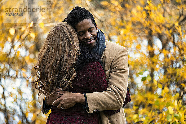 Nahaufnahme eines Paares gemischter Abstammung  das sich umarmt  während es bei einem Familienausflug im Herbst in einem Stadtpark schöne Zeit miteinander verbringt; Edmonton  Alberta  Kanada