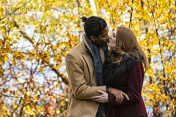 Ein gemischtrassiges Ehepaar umarmt und küsst sich  während es bei einem Familienausflug im Herbst in einem Stadtpark schöne Zeit miteinander verbringt; Edmonton  Alberta  Kanada