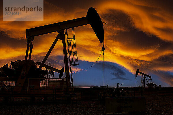 Silhouette von Pumpjacks vor einem farbenfrohen  dramatischen Sonnenuntergangshimmel mit warmen  leuchtenden Wolken  westlich von Airdrie; Alberta  Kanada