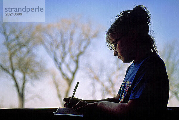 Mädchen schreibt draußen in einem Vogelschutzgebiet in ein Notizbuch; Gibbon  Nebraska  Vereinigte Staaten von Amerika