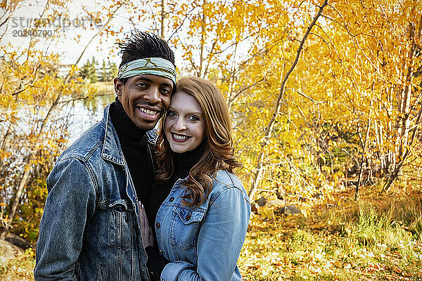 Nahaufnahme eines verheirateten Paares gemischter Abstammung  das sich umarmt und in die Kamera lächelt  während es bei einem Familienausflug im Herbst in einem Stadtpark schöne Zeit miteinander verbringt; Edmonton  Alberta  Kanada