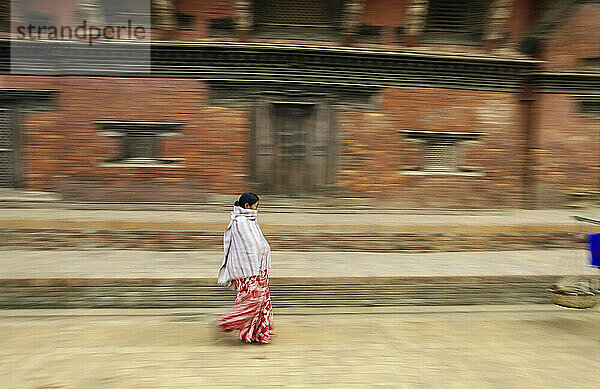 Schwenkansicht einer nepalesischen Frau  die an einem Backsteingebäude vorbeieilt; Kathmandu  Nepal
