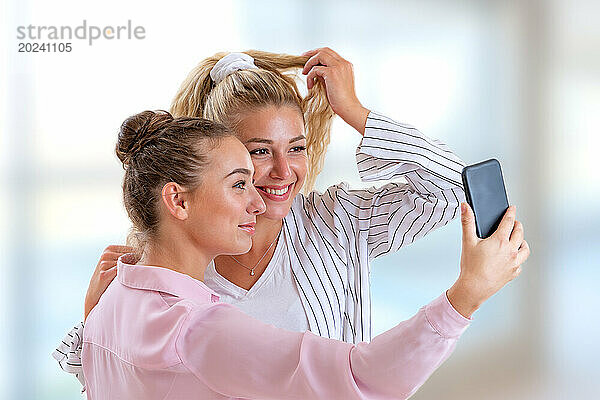 Zwei Freundinnen posieren für ein Selfie vor einem hellen und verschwommenen Hintergrund.