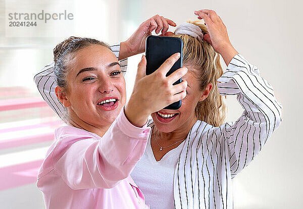 Zwei junge Frauen machen ein Selfie und lachen laut – heller  verschwommener Hintergrund.