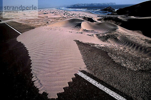 Sanddünen dringen auf den Pan American Highway an der Küste Perus vor  der von starken Küstenwinden von einem einsamen Strand aus geweht wird. Der asphaltierte  aber isolierte Abschnitt der Straße verläuft entlang der Küste in der Sechura-Wüste südlich von Casma  Peru. Der Panamerikanische Highway verbindet eine Vielzahl von Ländern und kulturellen Erlebnissen entlang des 10.000 Meilen langen Straßenabschnitts  der sich durch Lateinamerika erstreckt. Lebhafte  elegante Städte stehen in Mexiko  Peru und Chile im Kontrast zu einsamer Wüste und ländlicher Umgebung. Peru