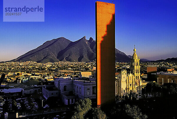 Blick auf die Landeshauptstadt Monterrey mit dem Naturdenkmal des Sattelbergs Cerro de la Silla im Kontrast zum orangefarbenen  modernen  monolithischen Turm von Faro Del Comercio (Leuchtturm des Handels) und der barocken  historischen Kathedrale von Monterrey in Macroplaza im Stadtzentrum; Monterrey  Nuevo León  Mexiko
