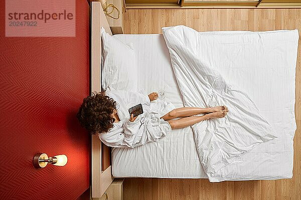 Draufsicht auf eine unerkennbare Frau  die ihre Beine im Bett mit einem Smartphone fotografiert