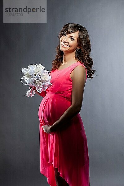 Bild einer elegant gekleideten schwangeren Frau  die in die Kamera lächelt