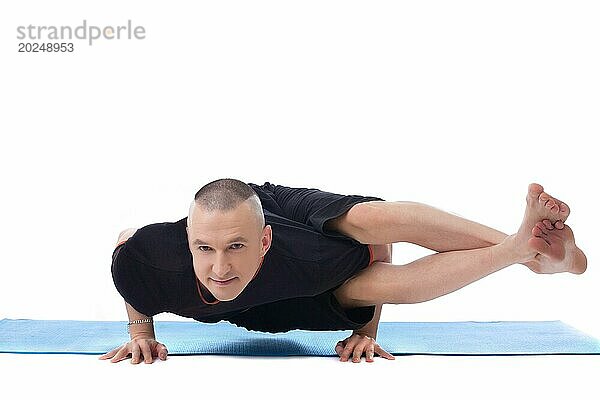 Lächelnder flexibler Mann in schwieriger Yogapose  vor weißem Hintergrund