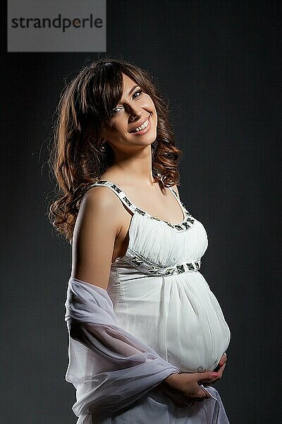 Glückliche schöne dunkelhaarige schwangere Frau lächelt in die Kamera