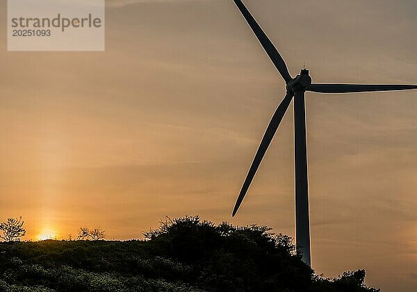 Silhouette einer Windturbine vor bewölktem Himmel  während die Sonne hinter einem Berggipfel in Südkorea untergeht