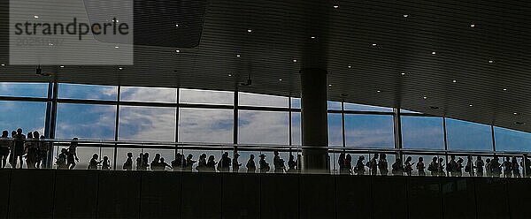 Silhouette von Menschen stehen in der Schlange auf der oberen Etage des Flughafens Gebäude vor dem blauen Himmel außerhalb Fenster in China