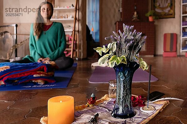 Mit Lavendelblüten und Räucherstäbchen geschmückter Meditationsaltar  im Hintergrund eine meditierende junge Frau  unscharf