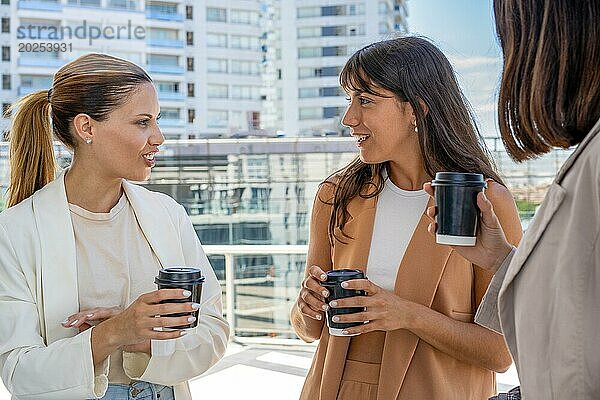 Drei Geschäftsfrauen stehen draußen und genießen ihre Büropause  lächeln und halten Tassen mit Kaffee. Konzept der Kameradschaft und Freundschaft  wie die Frauen einen Moment teilen  während sie ihre Getränke genießen