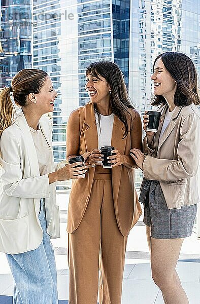 Drei Geschäftsfrauen stehen draußen vor einem Gebäude  genießen ihre Büropause  lächeln und halten Tassen mit Kaffee. Konzept der Kameradschaft und Freundschaft  wie die Frauen einen Moment teilen  während sie ihre Getränke genießen