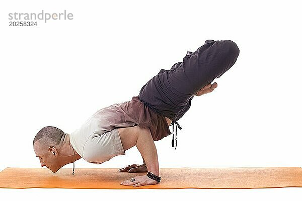 Konzentrierter athletischer Mann in schwieriger Yogapose  vor weißem Hintergrund