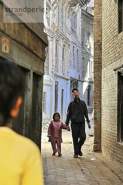 Ein Mann und ein kleines Mädchen laufen Hand in Hand durch eine enge Gasse  Kathmandu-Tal. Kathmandu  Nepal  Asien