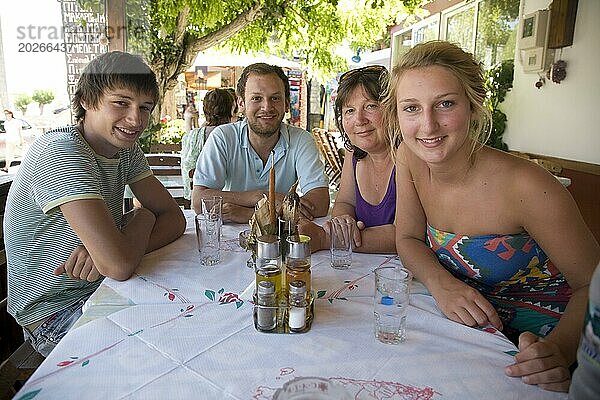 Model Familie mit Mutter und drei jungen erwachsenen Kindern  die im Urlaub in Griechenland um einen Tisch sitzen