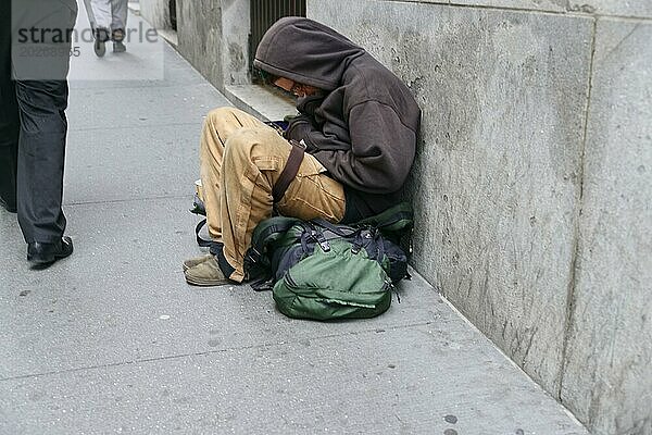 Ein obdachloser Mensch schläft zusammengerollt auf einem Gehweg  neben ihm ein grüner Rucksack  Manhattan  New York City  New York  USA  Nordamerika