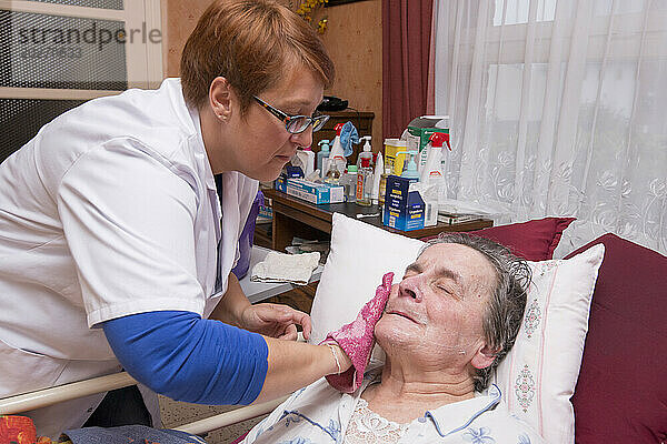HAD (Hospitalisierung zu Hause). Betreuung einer älteren Patientin zu Hause durch eine Pflegekraft. Toilettengang des behinderten älteren Menschen in seinem medizinischen Bett durch die Pflegekraft morgens nach dem Aufwachen.