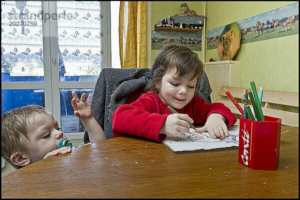 ASE – Sozialhilfe für Kinder. Sarah  3  zeichnet am Tisch  während Maxence versucht  ihr das Malbuch abzunehmen. NUR FÜR REDAKTIONELLE ZWECKE.