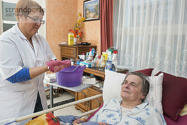 HAD (Hospitalisierung zu Hause). Betreuung einer älteren Patientin zu Hause durch eine Pflegekraft. Toilettengang des behinderten älteren Menschen in seinem medizinischen Bett durch die Pflegekraft morgens nach dem Aufwachen.