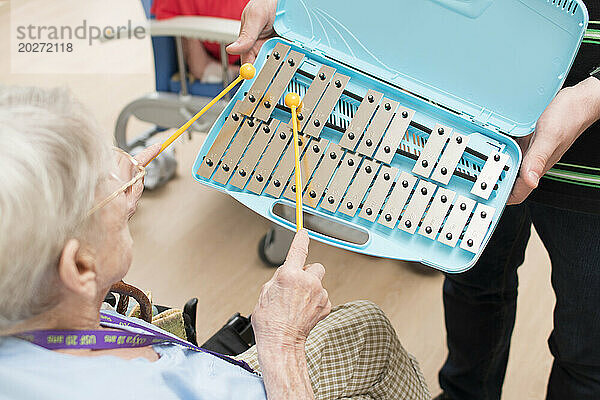 EHPAD – Älterer Bewohner klopft während einer musikalischen Aktivität auf ein Xylophon.