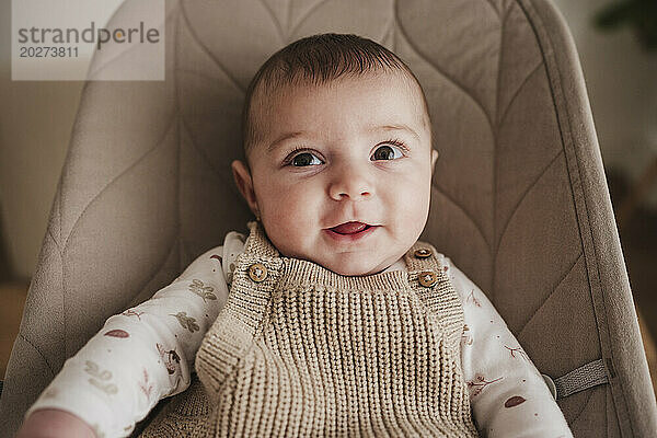 Fröhliches süßes Baby  das auf einem beigefarbenen Hüpfstuhl sitzt