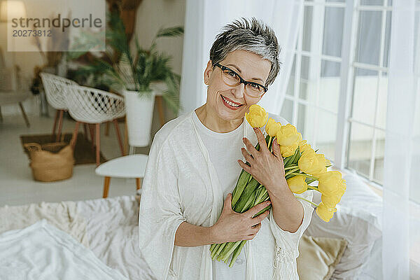 Lächelnde reife Frau hält einen Strauß Tulpen zu Hause