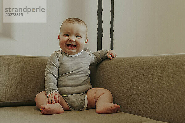 Happy baby boy sitting on sofa at home