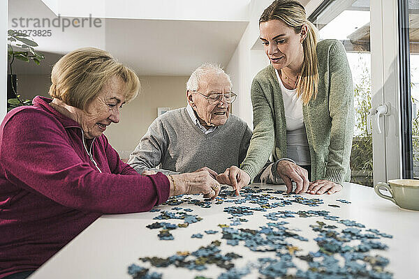 Heimpfleger mit älterem Paar  das am Tisch Puzzle spielt