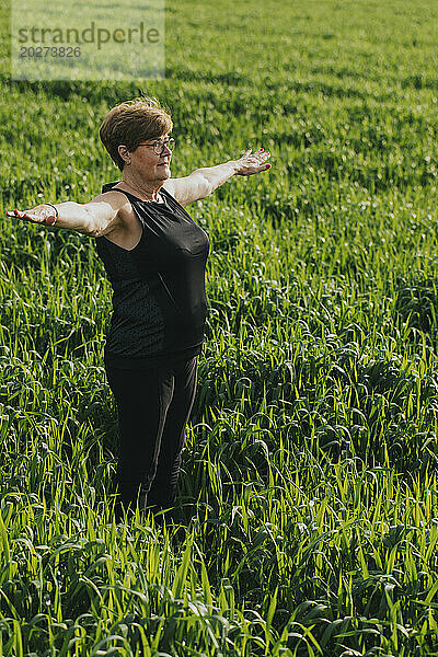 Senior woman exercising with arms outstretched in meadow