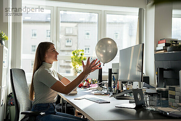 Sorglose Geschäftsfrau sitzt im Büro und spielt mit Luftballons