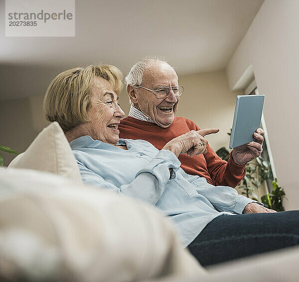 Fröhliches Seniorenpaar nutzt Tablet-PC im heimischen Wohnzimmer