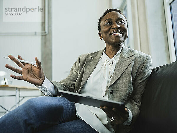 Lächelnde Geschäftsfrau hält Tablet-PC auf dem Sofa im Büro