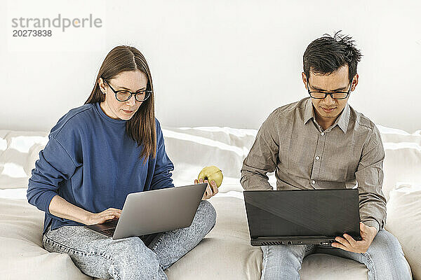 Diverse Programmierer sitzen mit Laptops auf dem Sofa im kreativen Startup-Büro