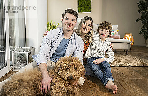 Glückliche Familie sitzt mit Hund im Wohnzimmer zu Hause