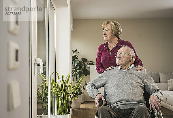 Ältere Frau kümmert sich um Mann  der zu Hause im Rollstuhl sitzt