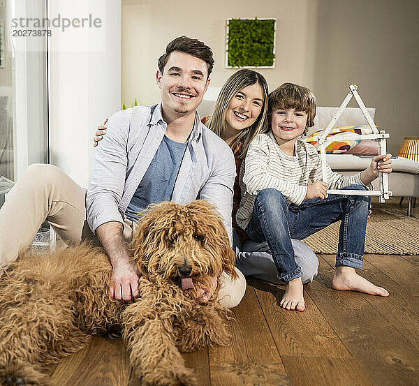 Glückliche Familie mit Musterhaus und Hund zu Hause