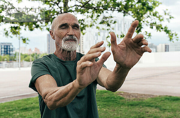 Aktiver älterer Mann trainiert mit geschlossenen Augen im Park