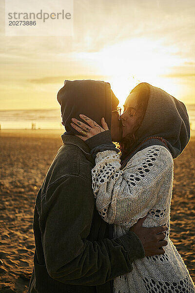 Junges Paar küsst sich bei Sonnenuntergang am Strand