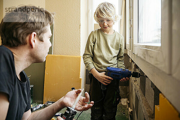 Reifer Vater bringt seinem Sohn bei  zu Hause Handwerkzeuge für die Renovierung zu verwenden