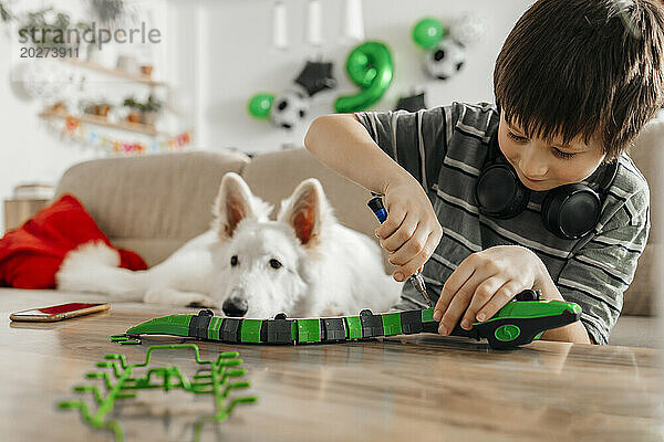 Junge baut Spielzeugschlangenmodell neben Hund zu Hause zusammen