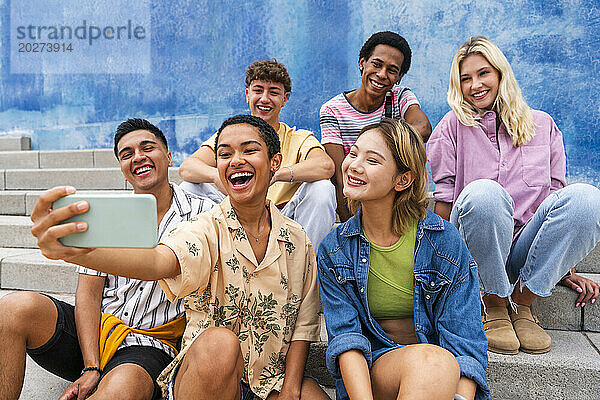 Fröhliche Gruppe junger Leute macht Selfie auf Stufen vor der Wand
