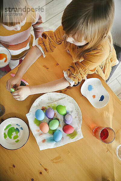 Girls coloring Easter eggs on table at home
