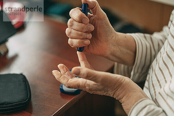 Ältere Frau sticht zu Hause in den Finger  um den Blutzuckerspiegel zu messen