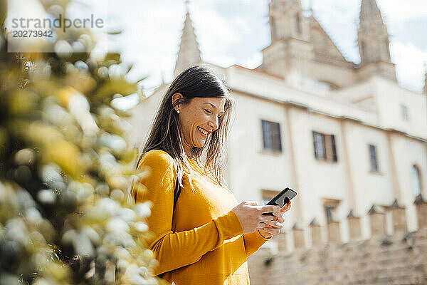 Glückliche Frau  die an einem sonnigen Tag ihr Smartphone in der Stadt benutzt
