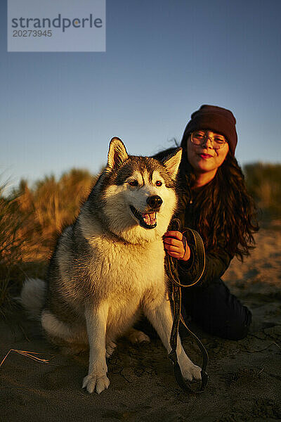 Lächelnde Frau  die bei Sonnenuntergang Spaß mit Hund hat